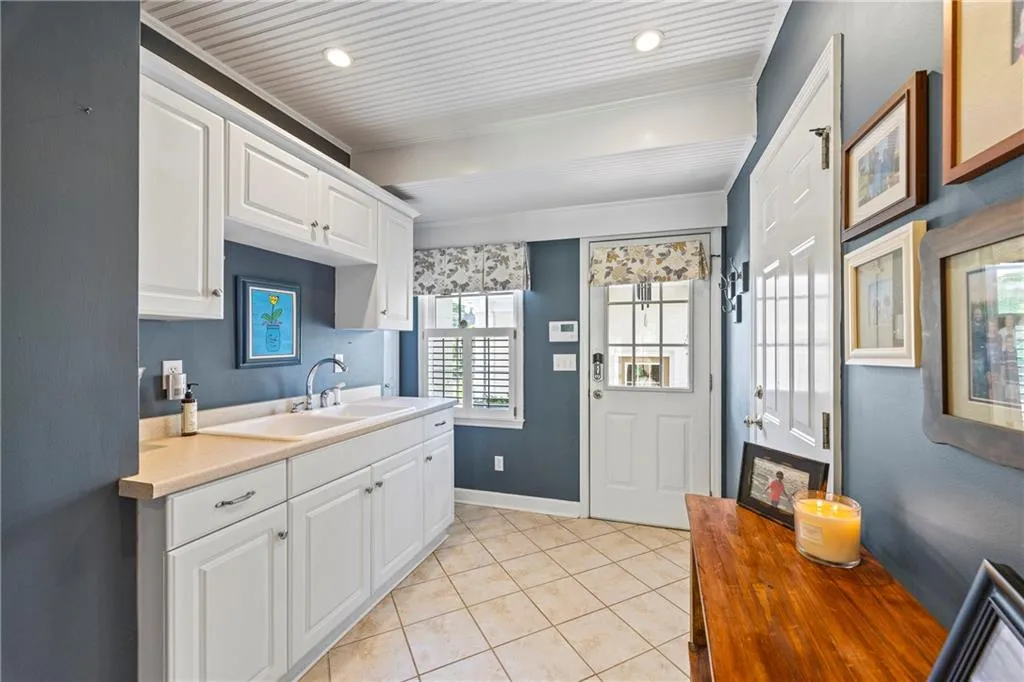 Kitchen with a sink, light tile patterned floors, white cabinetry, baseboards, and ornamental molding