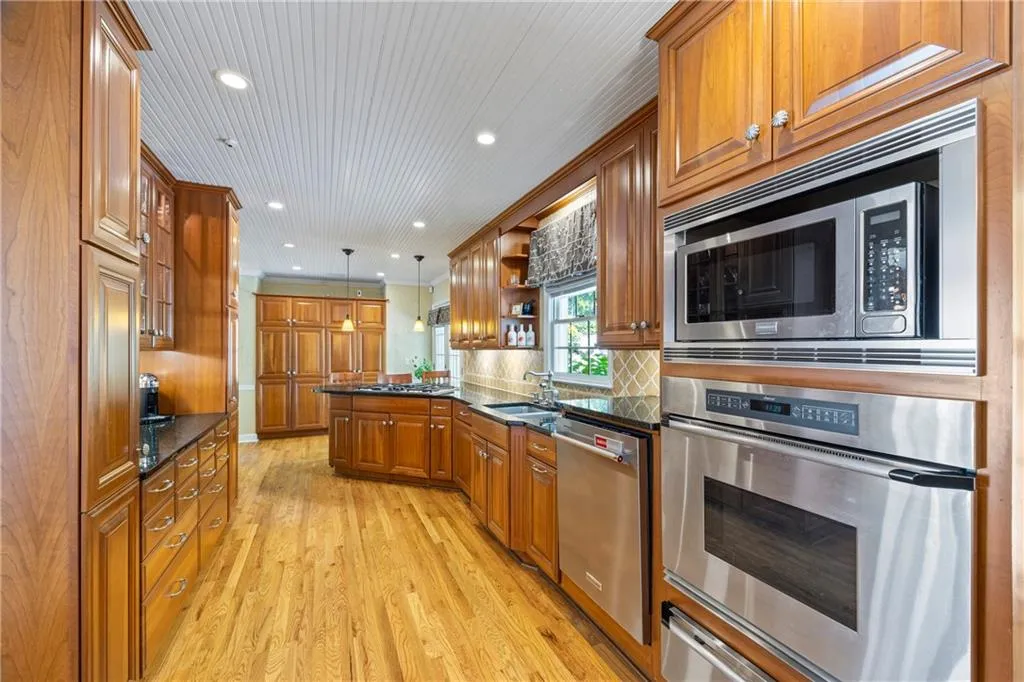 Kitchen with stainless steel appliances, open shelves, a warming drawer, light wood-style flooring, and brown cabinetry
