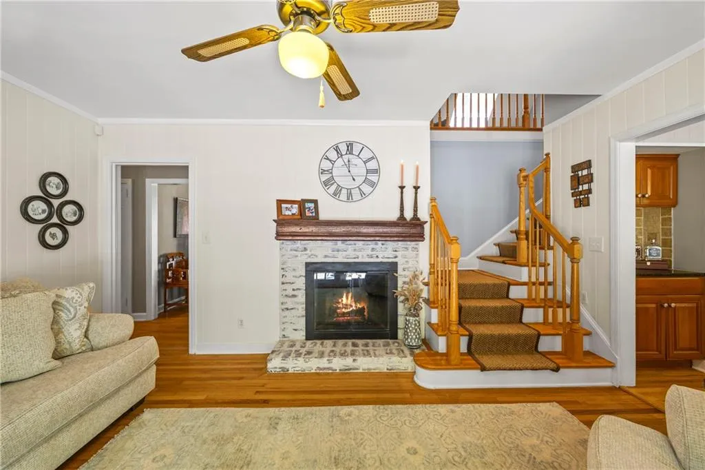 Living area with stairs, wood finished floors, ceiling fan, a fireplace, and ornamental molding