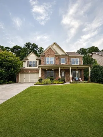 Brick facade with decorative gables, attached two-car garage, covered porch with columns, and a concrete driveway