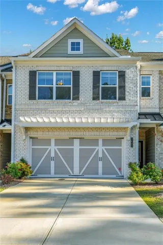 Brick exterior with contrasting siding, gabled roofline, decorative window shutters, and a two-car garage with carriage-style doors