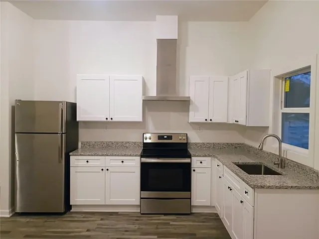 Kitchen featuring white shaker cabinetry, stainless steel appliances, granite-style countertops, and wood-finish flooring
