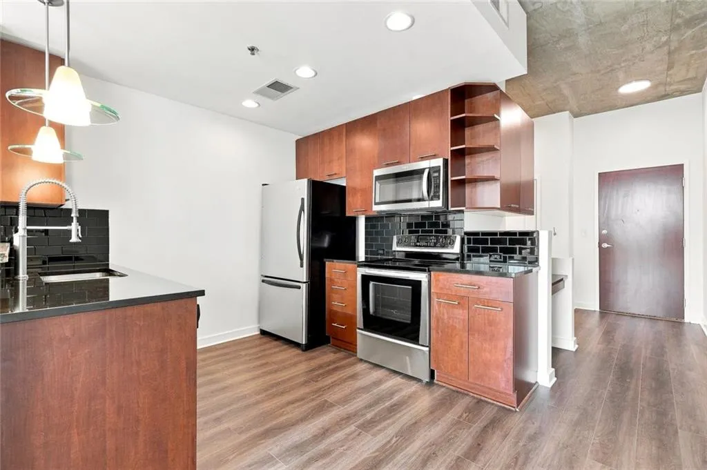 Kitchen featuring wood-finish flooring, stainless steel appliances, dark subway tile backsplash, recessed lighting, and a concrete ceiling