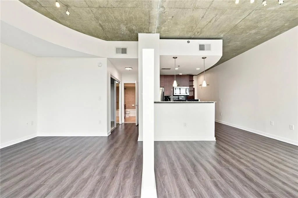 Exposed concrete ceiling, wood-finish flooring, track lighting, kitchen with pendant lights and breakfast bar