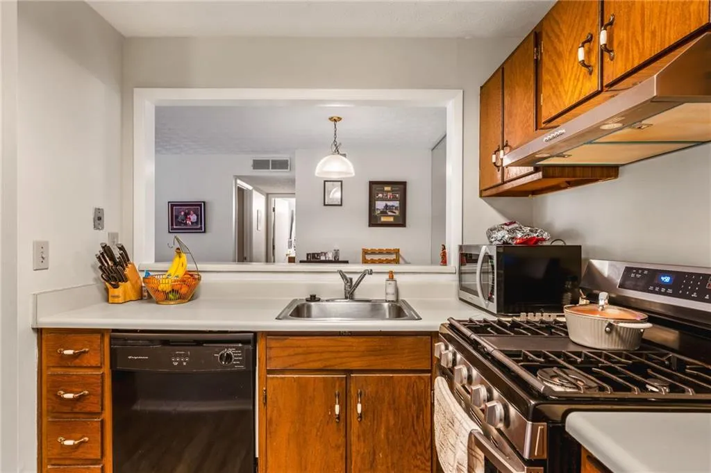 Kitchen with visible vents, brown cabinets, a sink, under cabinet range hood, and stainless steel appliances