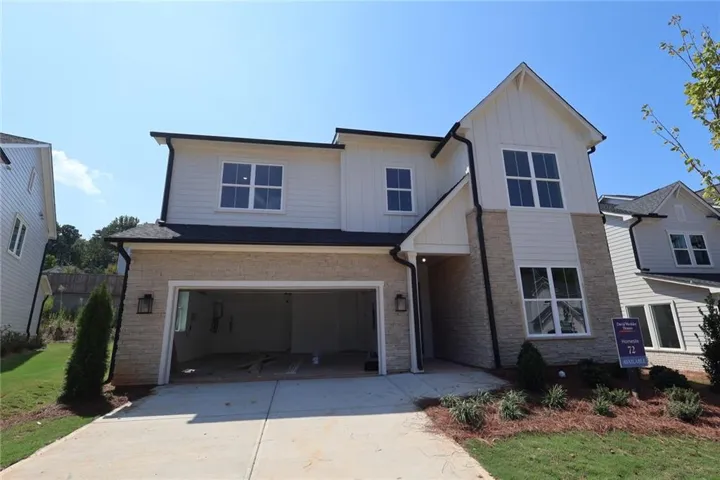 Two-story exterior with white siding and stone accents, featuring a two-car garage, prominent gabled roofline, and multiple windows