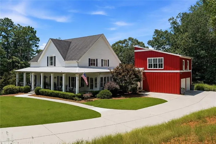 White two-story home with a wraparound porch, dark shutters, and a metal roof