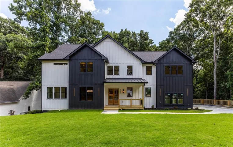 Modern farmhouse exterior with vertical board siding in contrasting dark and light tones, a covered front porch with natural wood railings, a dark shingle roof, and a meticulously manicured lawn