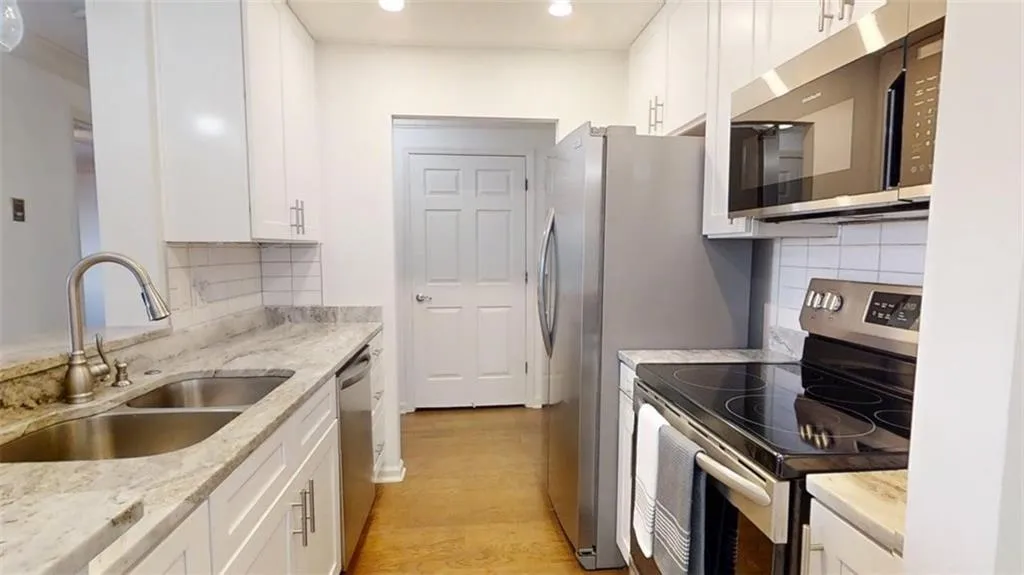Modern kitchen featuring light-toned countertops, white cabinetry with silver-toned hardware, and a stainless steel double basin sink with a pull-down faucet