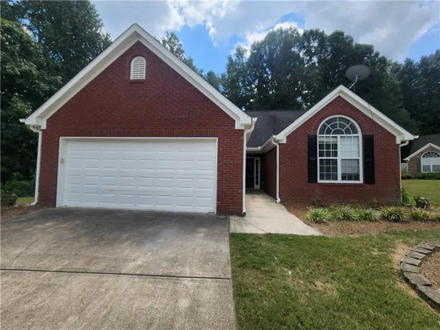 Brick exterior with a white garage door, arched window with black shutters, and mature landscaping