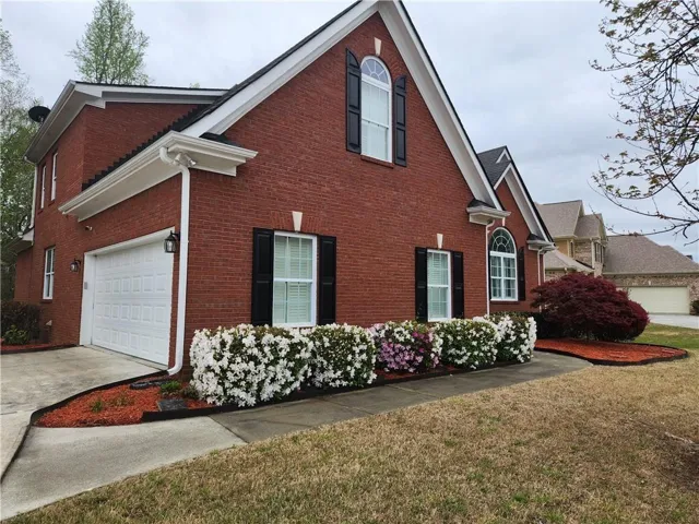 Brick exterior with white trim, arched window accents, black shutters, and mature landscaping