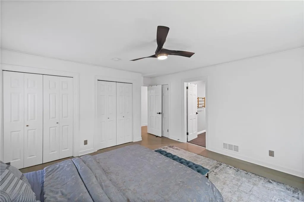 Bedroom with multiple closets, wood finished floors, a ceiling fan, and ensuite bath