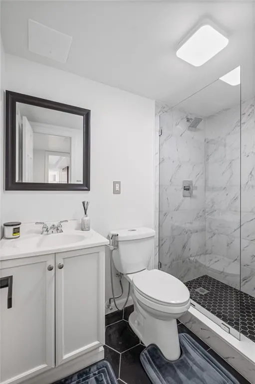 Full bath featuring vanity, a marble finish shower, and dark tile patterned flooring