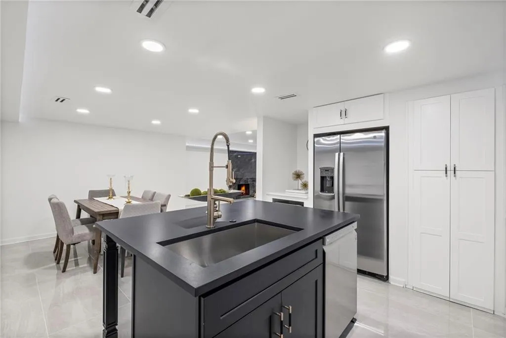 Kitchen with dark countertops, appliances with stainless steel finishes, an island with sink, light tile patterned flooring, and recessed lighting