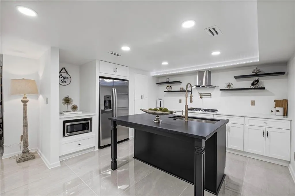 Kitchen with white cabinets, stainless steel appliances, open shelves, recessed lighting, and a kitchen island with sink