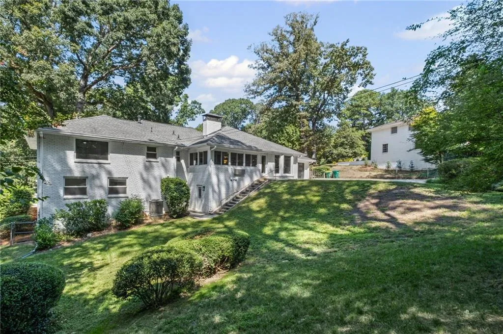 Back of house featuring stairway, a chimney, brick siding, and a lawn