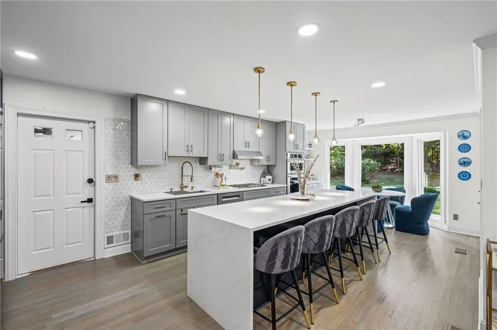 Kitchen featuring gray cabinets, a breakfast bar area, an island with sink, tasteful backsplash, and light stone counters
