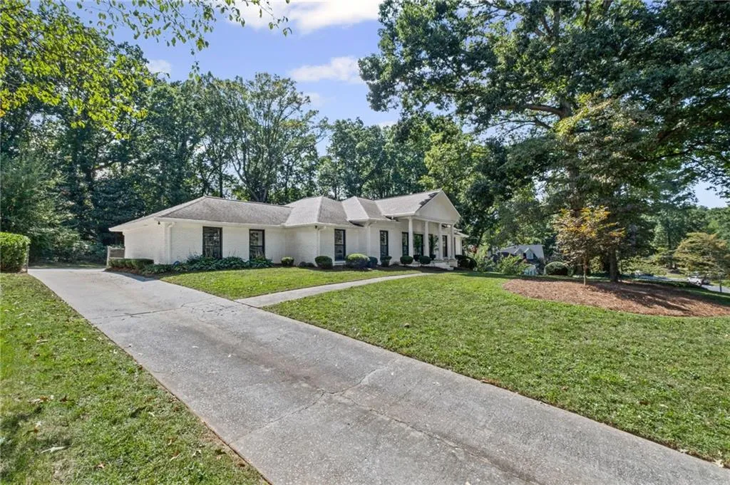 Ranch-style home with a front lawn, covered porch, view of scattered trees, and brick siding