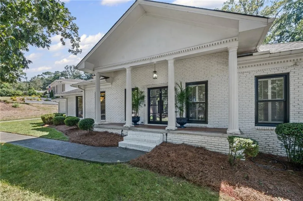 Doorway to property featuring covered porch, brick siding, and a lawn