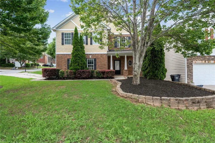 two-story home with mature trees, brick accents, and a charming front approach