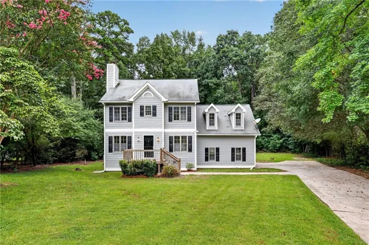 Two-story home with light gray siding, multiple dormer windows, and a front entry deck with railings