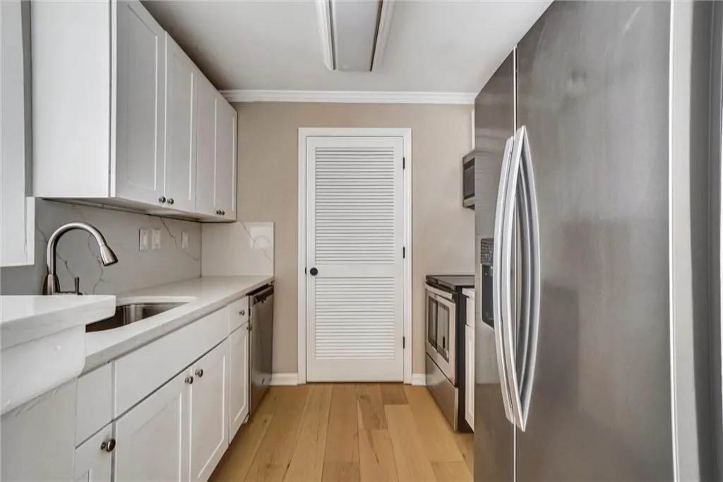 Kitchen featuring stainless steel appliances, white cabinets, light wood-type flooring, and light stone counters Kitchen featuring stainless steel appliances, white cabinets, light wood-type flooring, and light stone counters
