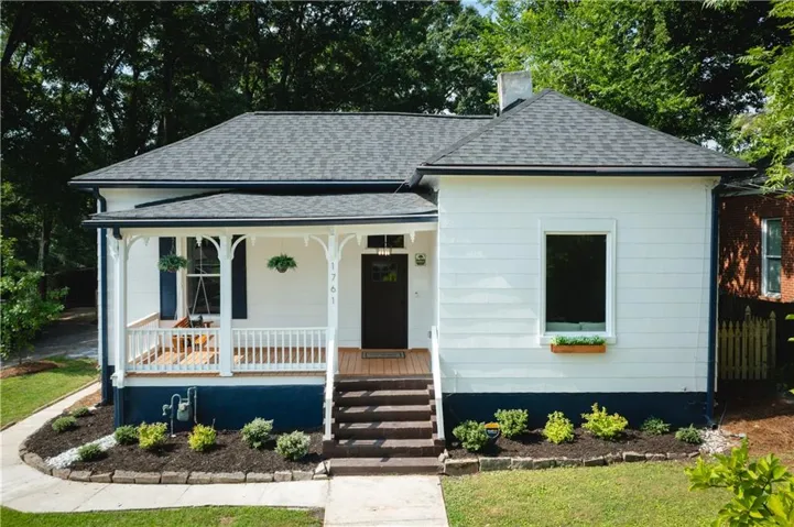 Charming single-story residence featuring a covered front porch with white railing, dark wood-finish steps, and a dark asphalt shingle roof