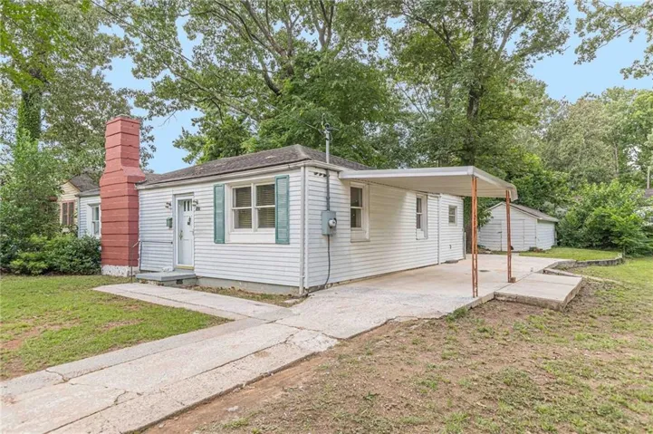 White siding exterior with a red brick chimney, blue shutters, and a covered concrete carport