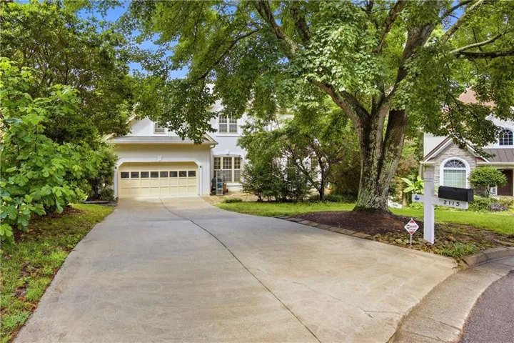White stucco residence with a two-car garage, featuring a concrete driveway and mature trees
