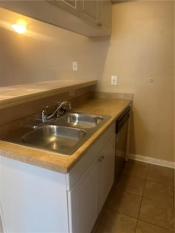 Kitchen with white cabinets, light countertops, light tile patterned floors, and dishwasher