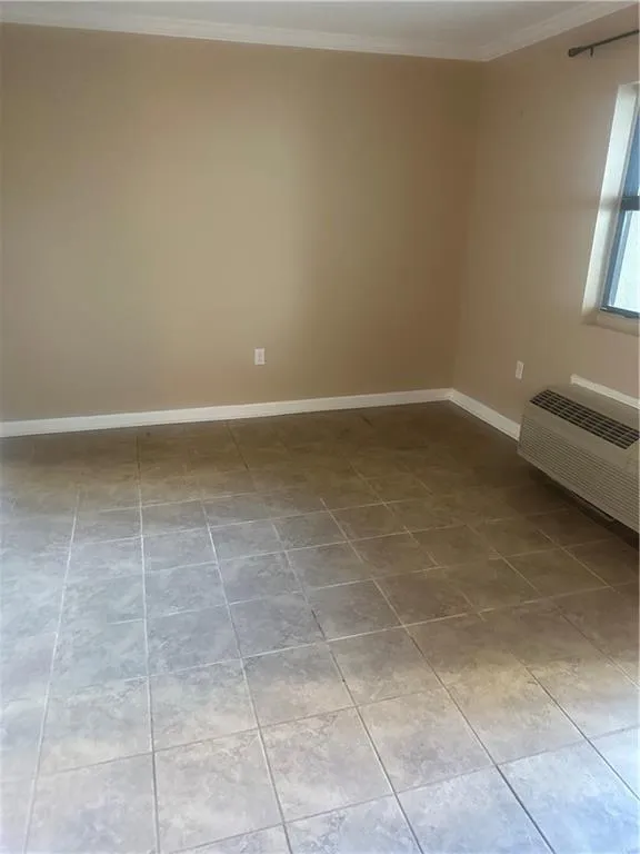 Unfurnished room featuring crown molding, a wall unit AC, and light tile patterned floors