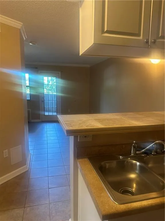 Kitchen featuring crown molding, a textured ceiling, light tile patterned floors, tile countertops, and white cabinets