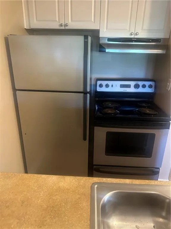 Kitchen with appliances with stainless steel finishes, exhaust hood, and white cabinets