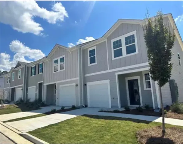 Modern townhome exterior featuring light gray siding with white trim, a single-car garage, and a dark entry door