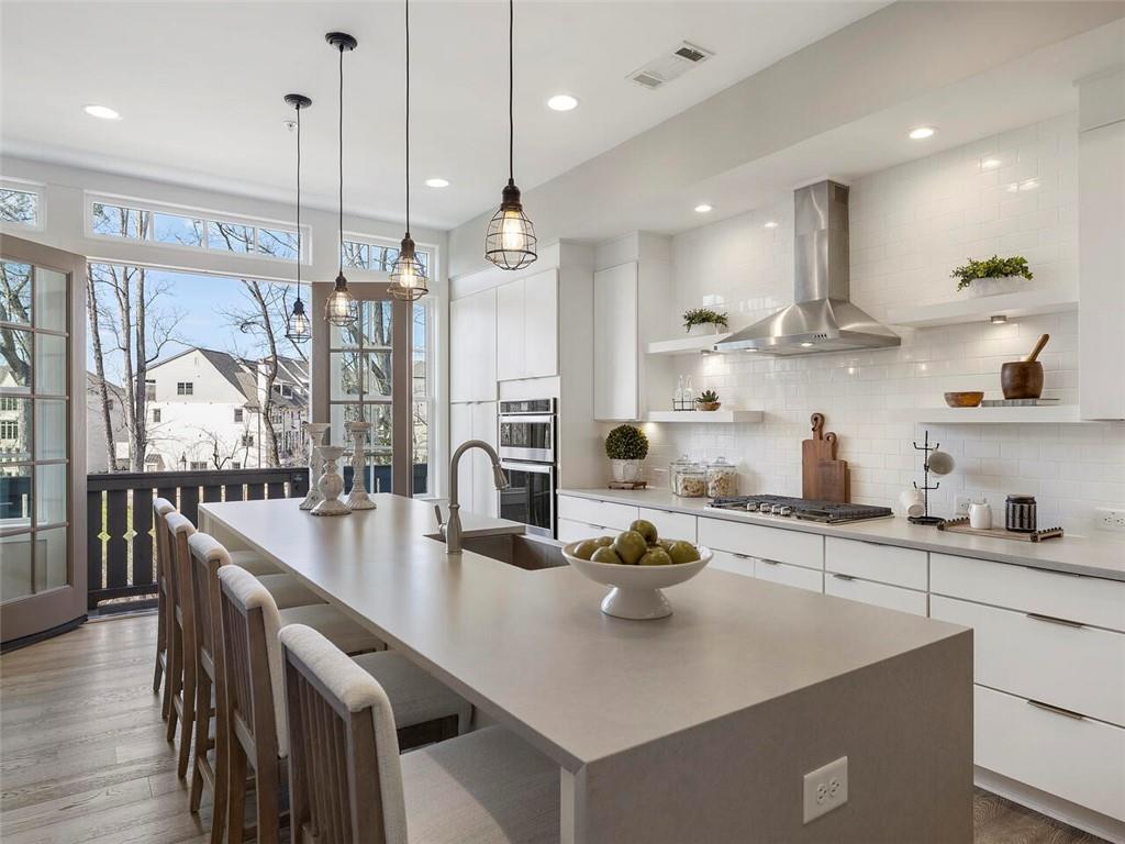 Kitchen with backsplash, an island with sink, hardwood / wood-style flooring, and wall chimney exhaust hood