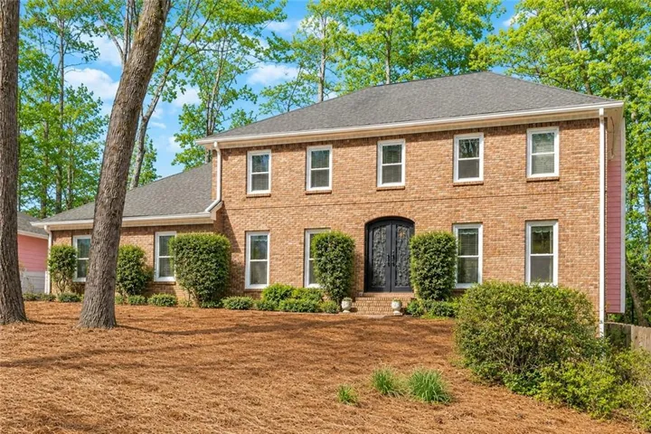 Two-story brick exterior featuring a dark gray shingle roof, double-paned windows with white frames, and a double-door main entry with decorative ironwork
