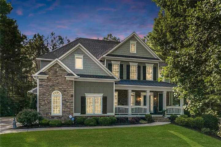 Multi-level home featuring stone and siding exterior, a covered porch with white columns, dark shutters, and a manicured front lawn