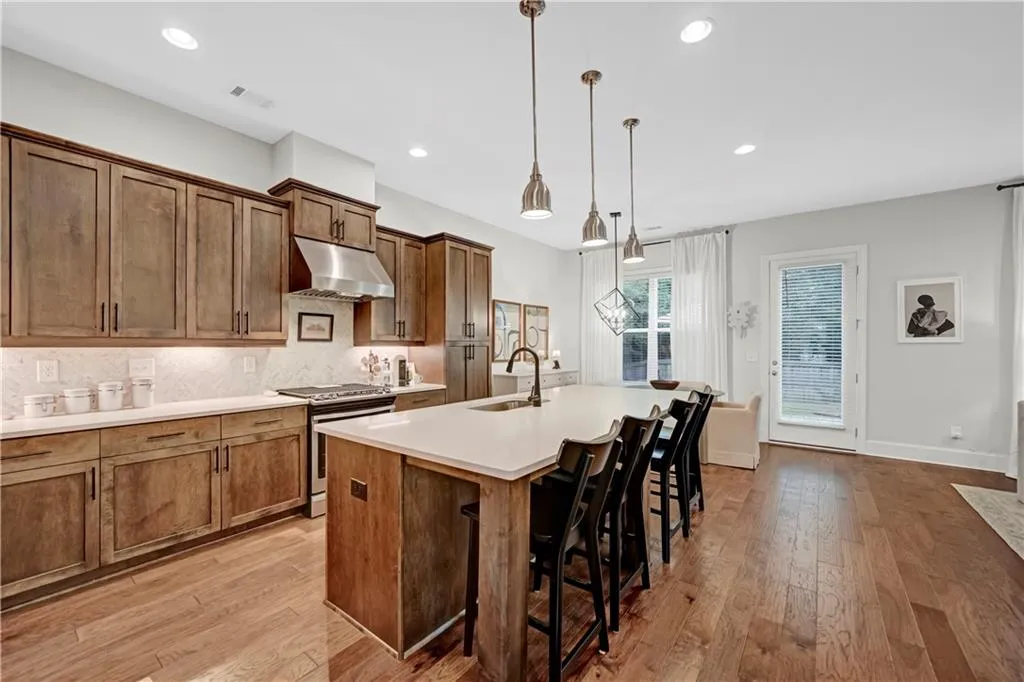 Kitchen featuring stainless steel stove, brown cabinetry, under cabinet range hood, backsplash, and a center island with sink