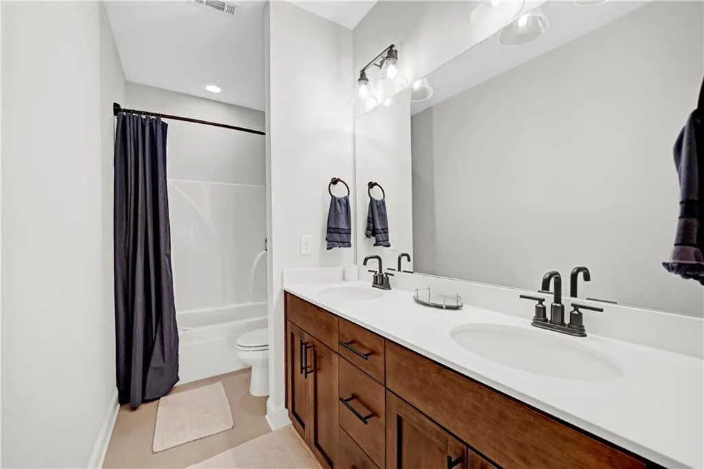 Bathroom featuring shower / bathtub combination with curtain, double vanity, and light tile patterned floors