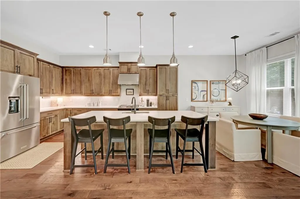 Kitchen featuring high end refrigerator, a kitchen breakfast bar, decorative light fixtures, a kitchen island with sink, and light wood finished floors