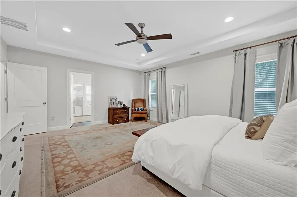 Bedroom featuring a raised ceiling, ceiling fan, carpet flooring, recessed lighting, and connected bathroom