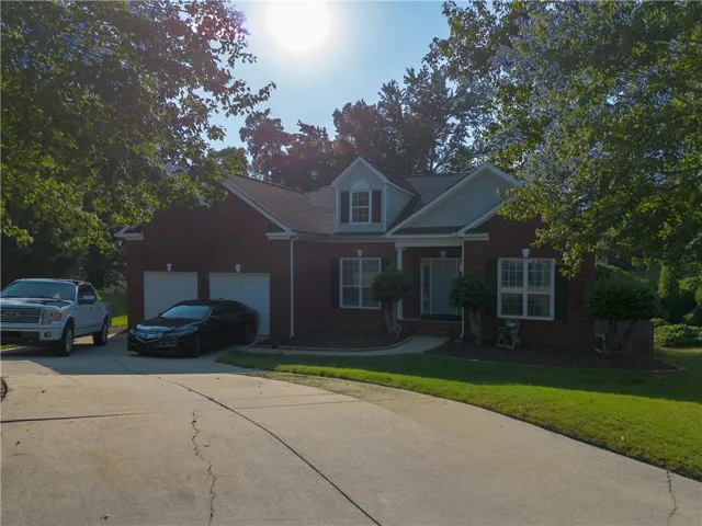 Brick exterior with white trim, two-car garage, mature trees, concrete driveway, and a front porch