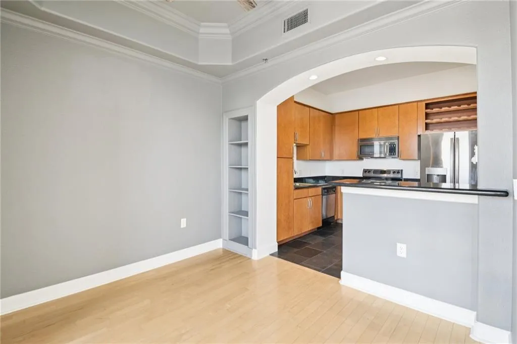 Kitchen featuring dark countertops, open shelves, brown cabinetry, appliances with stainless steel finishes, and ornamental molding