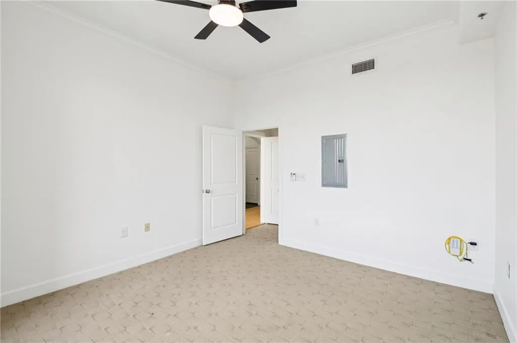 Carpeted spare room with crown molding, electric panel, and ceiling fan
