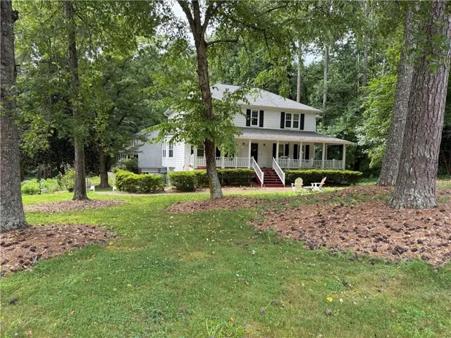 White two-story residence featuring a covered front porch with white railings, dark shutters, and a red-toned staircase
