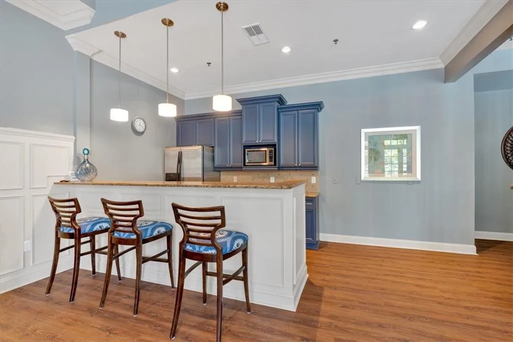 Kitchen featuring wood finished floors, light stone countertops, crown molding, appliances with stainless steel finishes, and a breakfast bar area