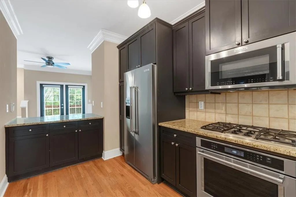 Kitchen with light stone counters, crown molding, tasteful backsplash, stainless steel appliances, and light wood finished floors