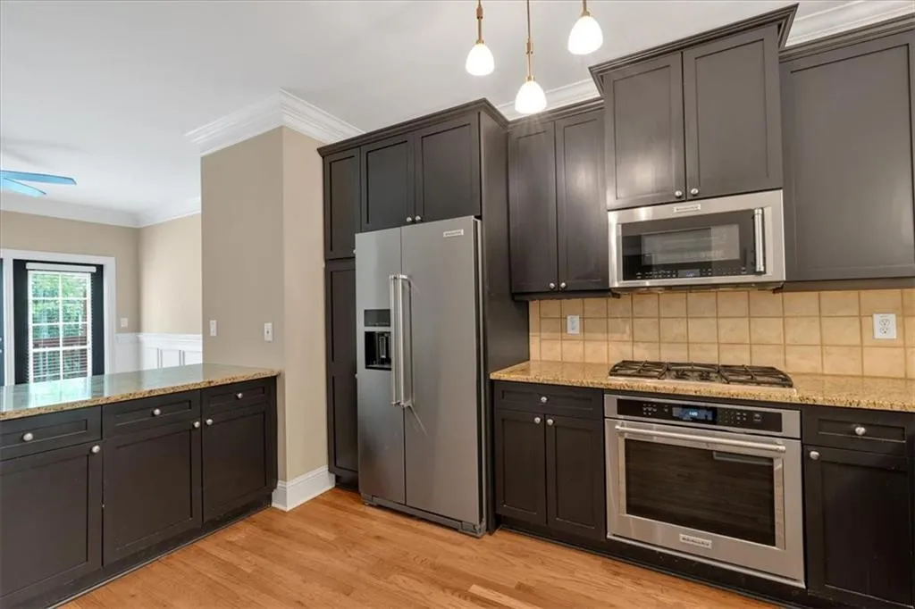 Kitchen with light wood-style flooring, tasteful backsplash, light stone counters, crown molding, and appliances with stainless steel finishes