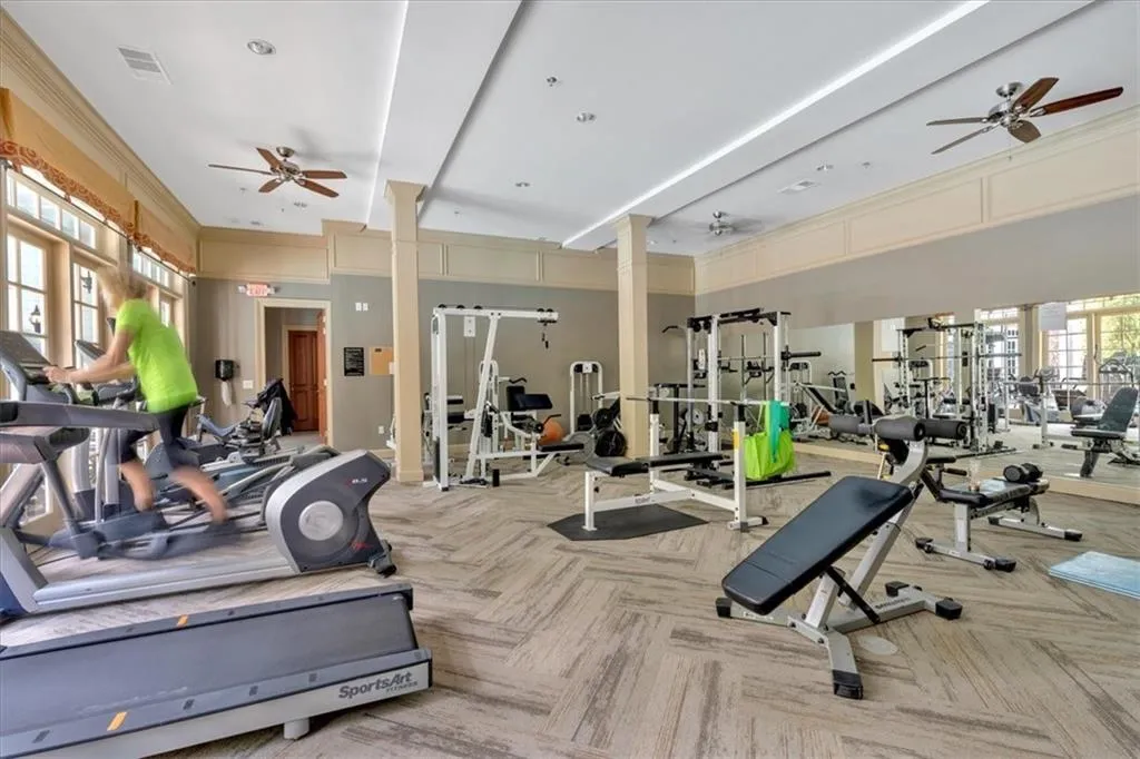 Gym featuring decorative columns, visible vents, carpet, and a ceiling fan