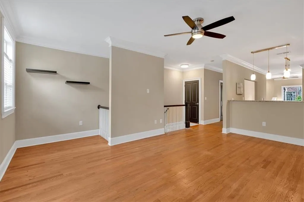 Unfurnished living room featuring light wood-type flooring, a ceiling fan, baseboards, and crown molding